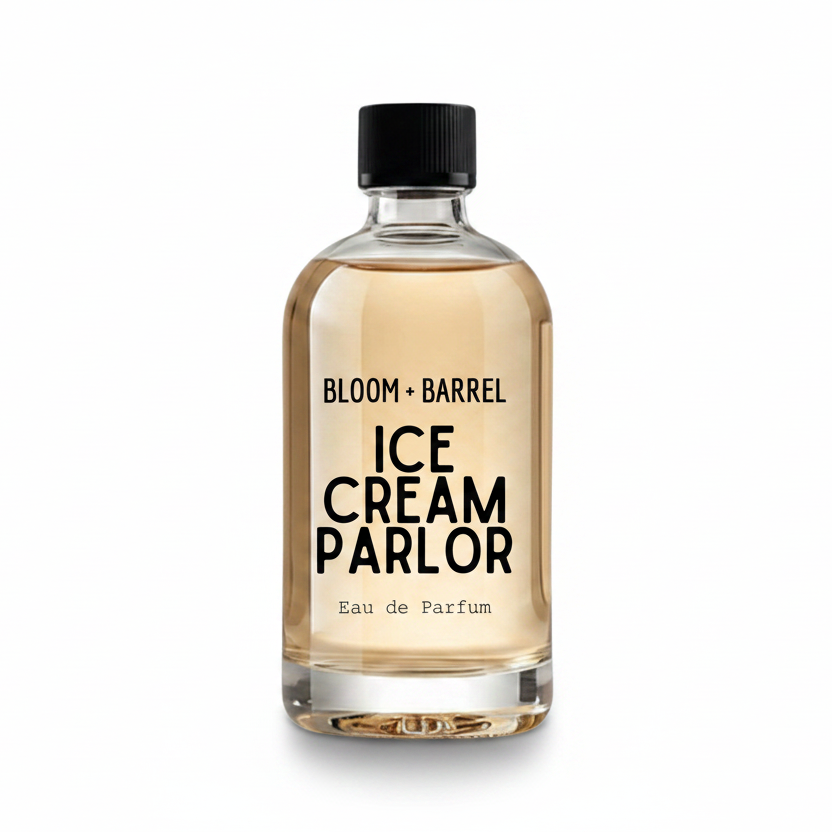 A clear glass perfume bottle with a black cap, filled with a pale amber liquid. The bottle features a white label with black text reading 'BLOOM + BARREL' and 'ICE CREAM PARLOR Eau de Parfum'.