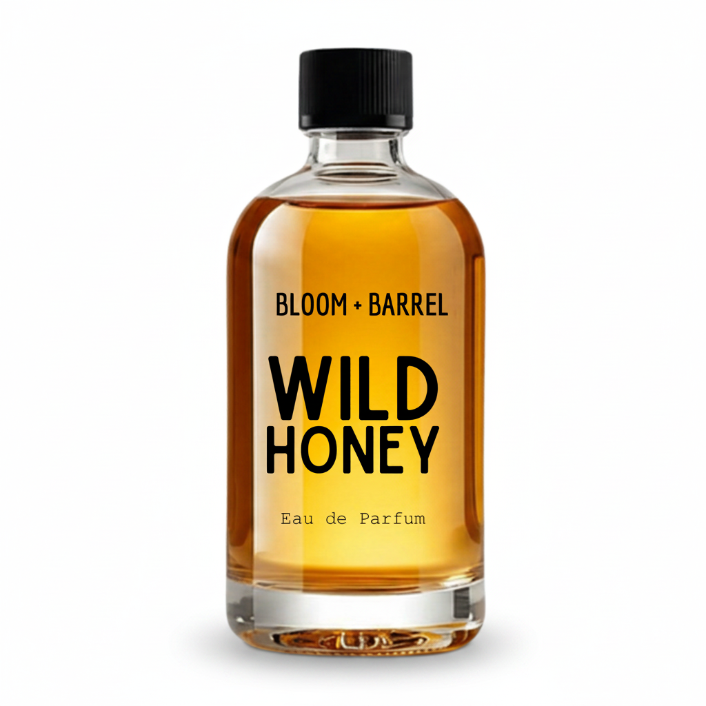 A clear glass bottle of Bloom + Barrel Wild Honey Eau de Parfum with amber-colored liquid, a black cap, and bold black text on a white background.