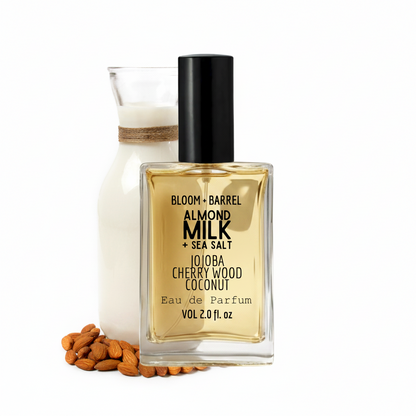 Perfume bottle labeled 'Almond Milk & Sea Salt' with a small container and almonds on a white background