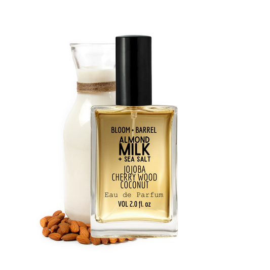 Perfume bottle labeled 'Almond Milk & Sea Salt' with a small container and almonds on a white background