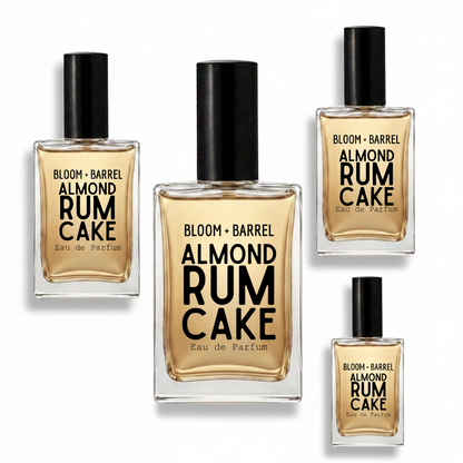 Four clear glass perfume bottles with black caps and amber-gold liquid, arranged on a white background. The bottles are labeled BLOOM + BARREL ALMOND RUM CAKE Eau de Parfum, with sizes shown in different bottle scales.