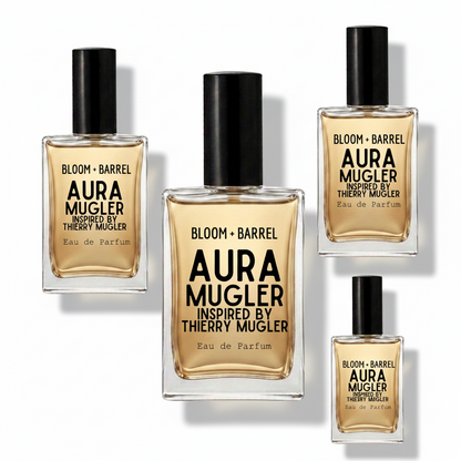 Four glass perfume bottles with black caps from Aura Mugler Bloom + Barrel collection, arranged on a plain white background. The bottles contain a warm amber liquid and feature black text labels.