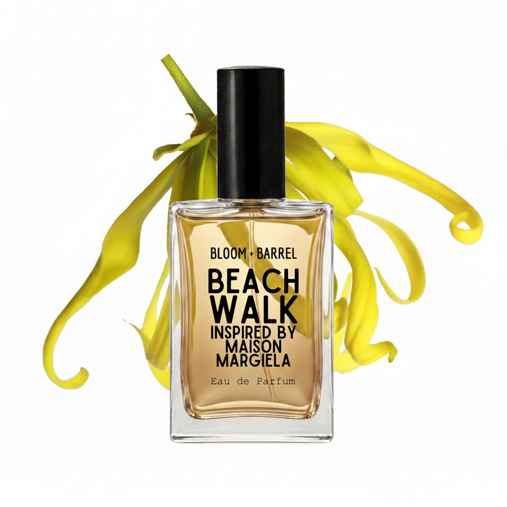 A bottle of Bloom + Barrel Beach Walk Eau de Parfum, inspired by Maison Margiela, featuring amber-colored liquid in a clear glass bottle with a black cap, set against a white background with yellow flower petals.