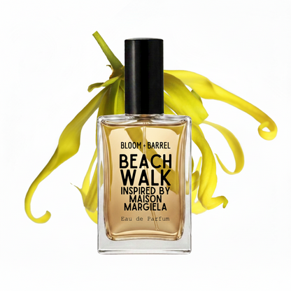 A bottle of Bloom + Barrel Beach Walk Eau de Parfum, inspired by Maison Margiela, featuring amber-colored liquid in a clear glass bottle with a black cap, set against a white background with yellow flower petals.
