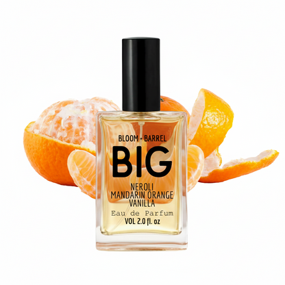 A bottle of Bloom + Barrel Big Neroli Mandarin Orange Vanilla Eau de Parfum, featuring a clear glass bottle with golden-yellow liquid, a black cap, and orange slices on a white background.