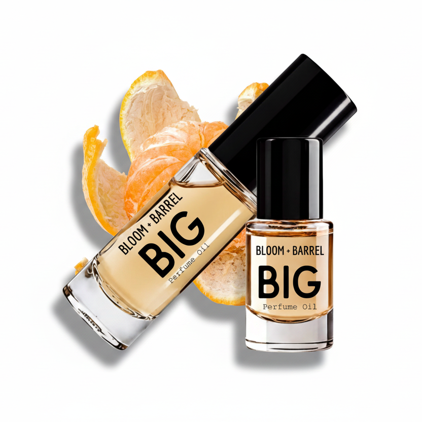 Two glass bottles of BLOOM + BARREL BIG Perfume Oil with black caps, one upright and one tilted, shown with orange peel slices on a white background.