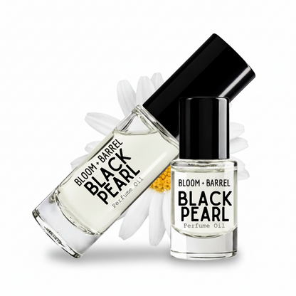 Two glass bottles of BLOOM + BARREL Black Pearl Perfume Oil with black caps, one larger diffuser bottle and one smaller spray bottle, displayed with white daisy petals on a white background.