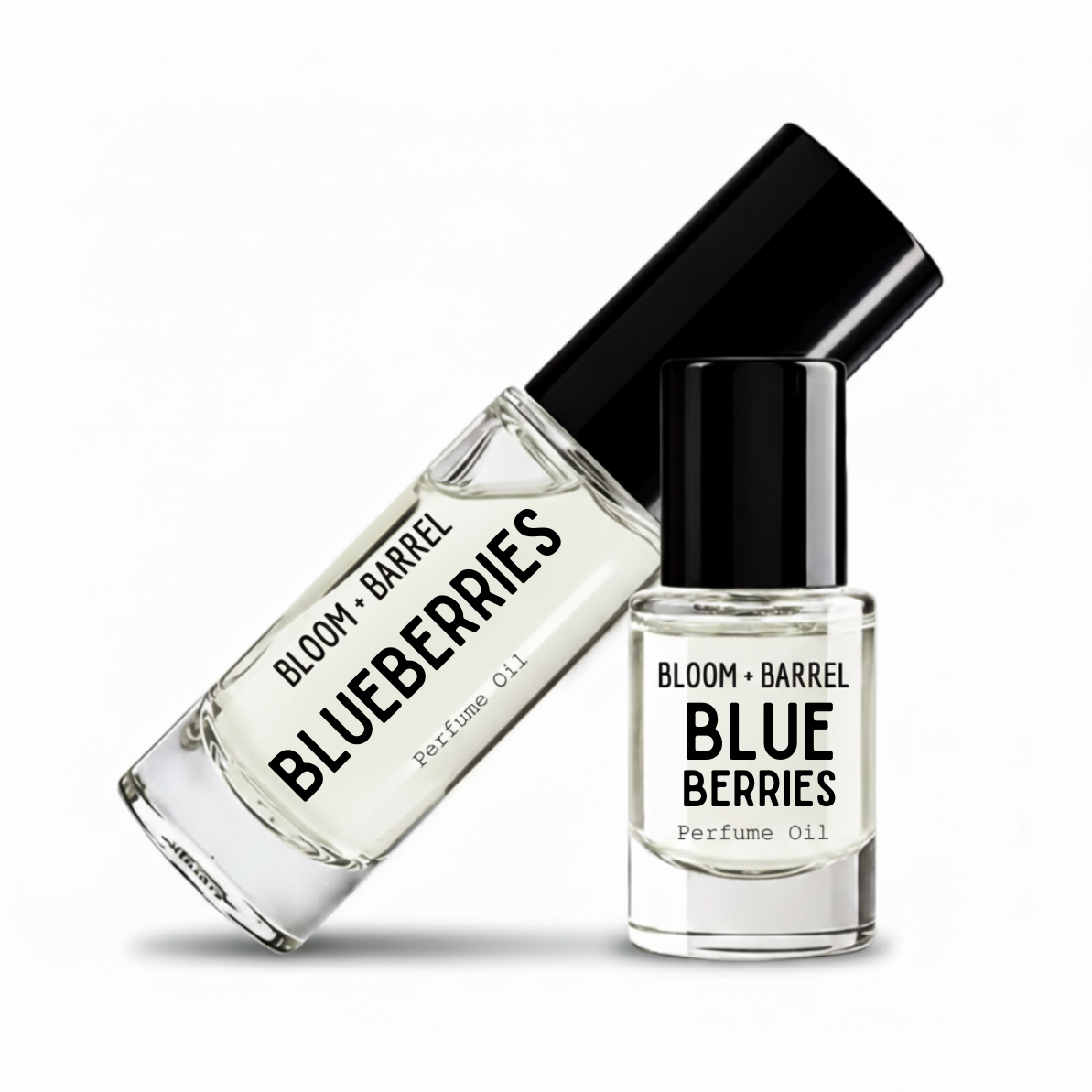 Two clear glass perfume oil bottles with black caps on a white background. One bottle is tilted diagonally and reads 'BLOOM + BARREL BLUEBERRIES Perfume Oil', while the other stands upright with the same label.
