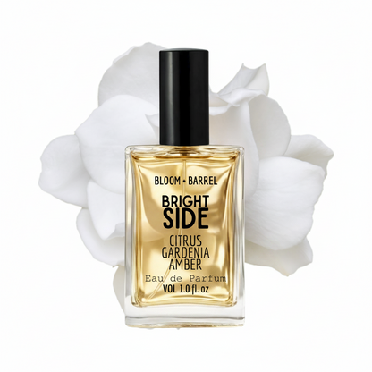 Perfume bottle labeled 'Bloom + Barrel Bright Side' with white flowers in the background