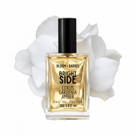 Perfume bottle labeled 'Bloom + Barrel Bright Side' with white flowers in the background