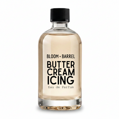 A clear glass perfume bottle filled with pale warm beige liquid, featuring a black ribbed cap and bold black text reading 'BLOOM + BARREL BUTTER CREAM ICING Eau de Parfum' on the front, shown on a plain white background.