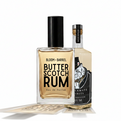 Two bottles of rum perfume on a plain white background: a square clear bottle labeled 'BLOOM • BARREL Butter Scotch Rum' with a black cap, and a taller clear bottle labeled 'Blackmate Spirits Butter Scotch Rum' with a black-and-white illustrated label and silver cap.