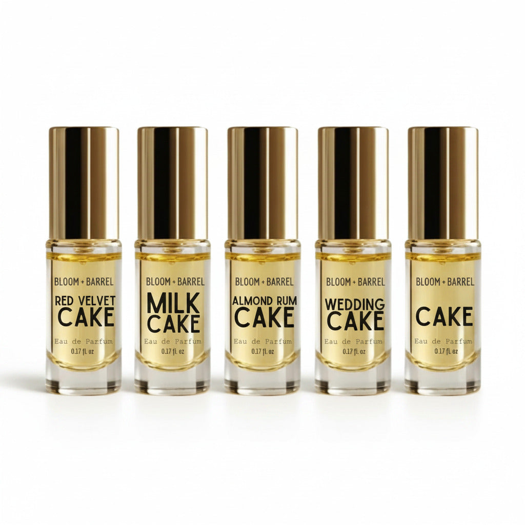 Six small Bloom + Barrel perfume sample bottles with metallic gold caps arranged in a row on a white background. The labels show different scent names: Red Velvet Cake, Milk Cake, Almond Rum Cake, Wedding Cake, and Birthday Cake.