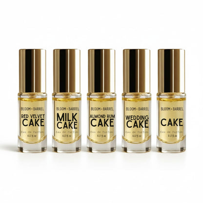 Six small Bloom + Barrel perfume sample bottles with metallic gold caps arranged in a row on a white background. The labels show different scent names: Red Velvet Cake, Milk Cake, Almond Rum Cake, Wedding Cake, and Birthday Cake.