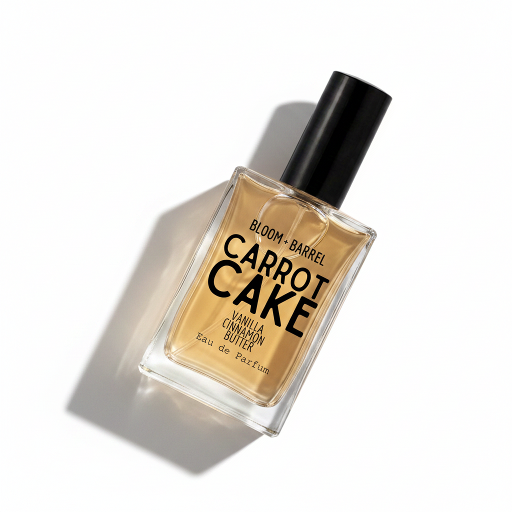 A rectangular glass perfume bottle with a black cap, filled with a warm amber liquid. The front label reads 'BLOOM • BARREL CARROT CAKE VANILLA CINNAMON BUTTER Eau de Parfum' in black text, set against a plain white background.