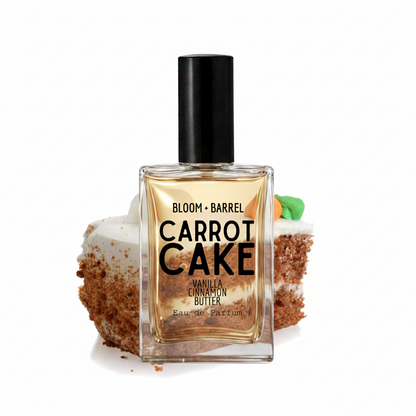 A perfume bottle labeled 'BLOOM + BARREL CARROT CAKE Vanilla Cinnamon Butter' stands centered in front of a sliced carrot cake on a white background.