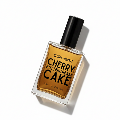 A rectangular glass bottle of Bloom Barrel Cherry Buttercream Cake Eau de Parfum with a black cap, filled with amber-colored liquid, set against a plain white background.