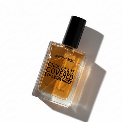 A rectangular glass bottle of Bloom Barrel 'Chocolate Covered Strawberries' Eau de Parfum, filled with amber-colored liquid and featuring a black cap, set against a plain white background.