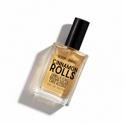 Bloom Barrel Cinnamon Rolls Eau de Parfum in a clear rectangular glass bottle with a black cap, filled with warm amber-brown liquid, on a plain white background.