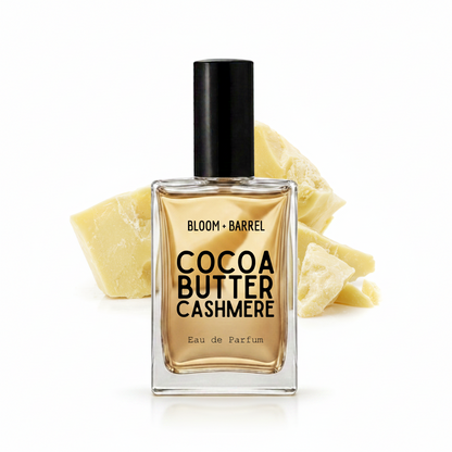 A bottle of Bloom Barrel Cocoa Butter Cashmere Eau de Parfum with a black cap, set against a white background with decorative cashmere wool chunks behind it.