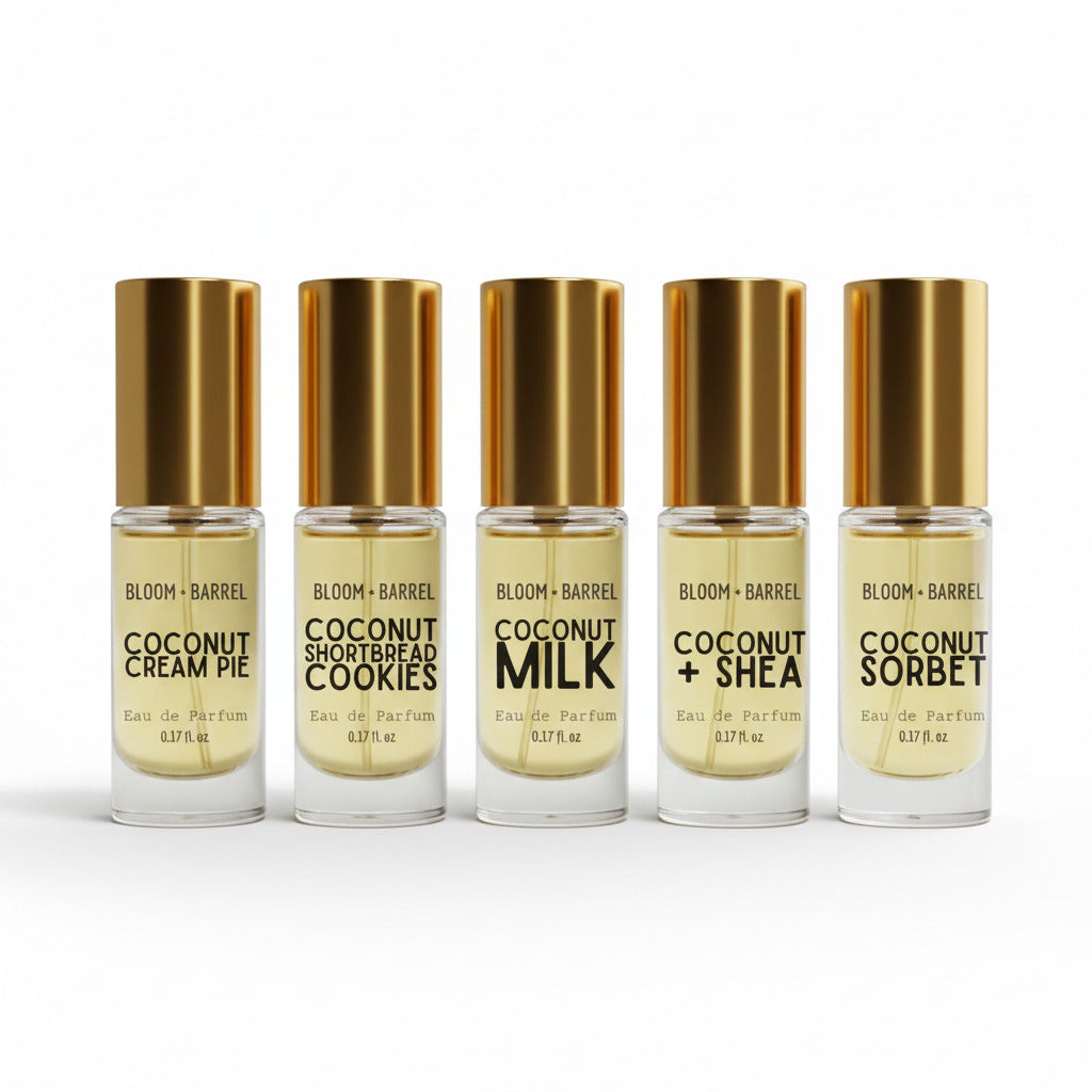 Five small clear glass bottles with metallic gold caps and gold-toned liquid, arranged in a row on a white background. The labels read Bloom + Barrel and various coconut-flavored variants including Cream Pie, Shortbread Cookies, Milk, + Shea, and Sorbet.