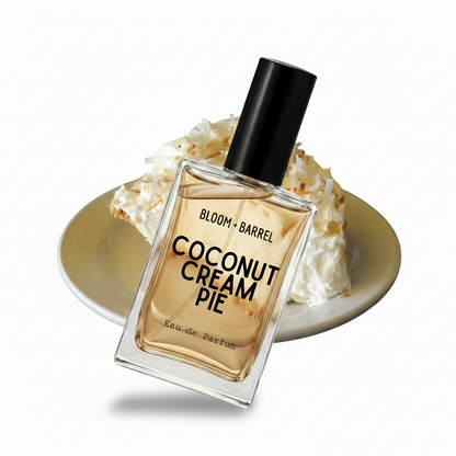 A perfume bottle labeled 'BLOOM • BARREL COCONUT CREAM PIE' with a black cap, placed in front of a plate of coconut cream pie on a white background.