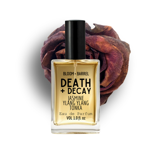 Perfume bottle labeled 'Death + Decay' with a dried rose on a white background
