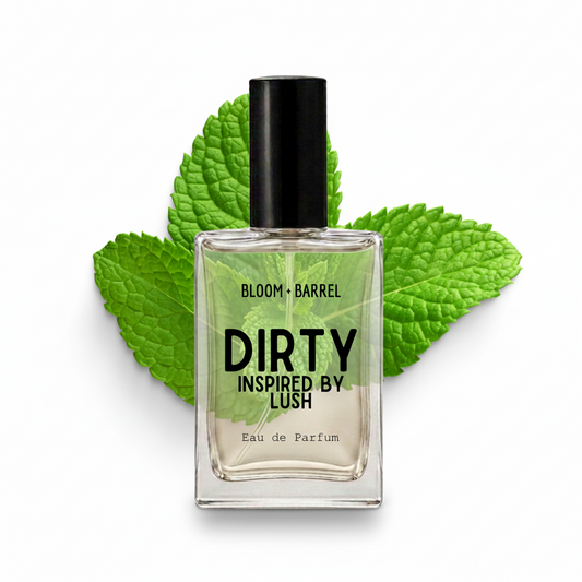 A clear glass perfume bottle with a black cap and black text reading 'DIRTY INSPIRED BY LUSH' and 'BLOOM • BARREL', centered in front of bright green mint leaves on a white background.