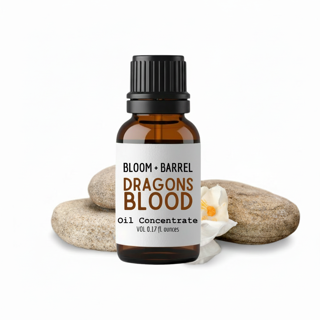 Bottle of Bloom & Barrel Dragons Blood oil concentrate with a label, surrounded by stones and a candle on a white background.