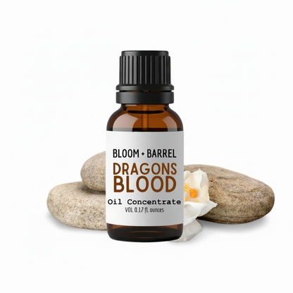 Bottle of Bloom & Barrel Dragons Blood oil concentrate with a label, surrounded by stones and a candle on a white background.