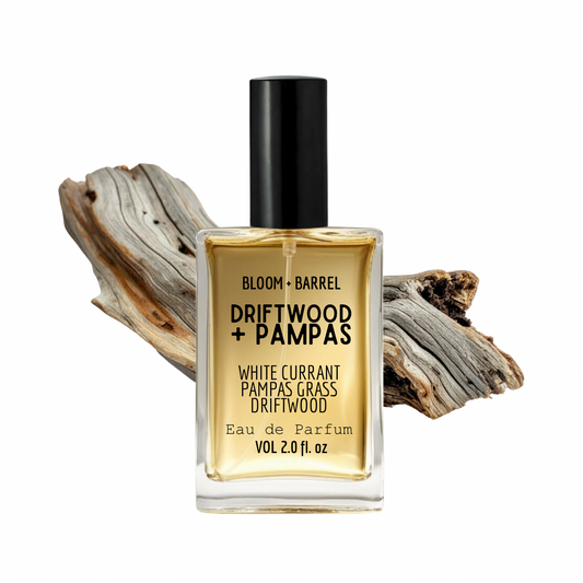 Perfume bottle labeled 'Driftwood + Pampas' with a piece of driftwood on a white background