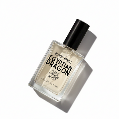 A rectangular glass perfume bottle with a black cap, labeled 'BLOOM • BARREL EGYPTIAN DRAGON CLOVE SAFFRON AMBER Eau de Parfum', centered on a plain white background.