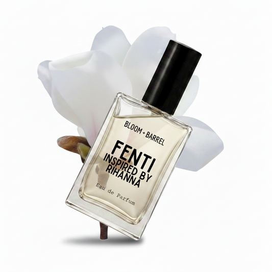 A clear rectangular perfume bottle with a black cap, labeled 'BLOOM • BARREL' and 'FENTI INSPIRED BY RIHANNA', centered against a white background with soft white flower petals behind it.