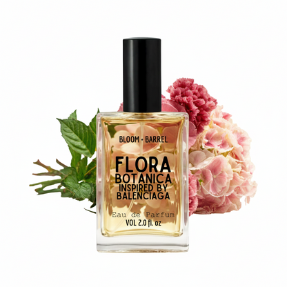 Balenciaga Bloom + Barrel Flora Botanica Eau de Parfum bottle with a black cap, filled with golden-yellow liquid, styled with pink flowers and green leaves on a white background.