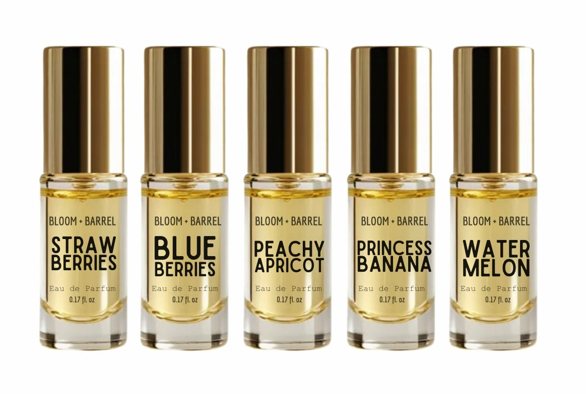 Six small Bloom + Barrel eau de parfum bottles with gold caps and clear glass, arranged side by side on a white background. Labels read Strawberry, Blueberries, Peachy Apricot, Princess Banana, and Watermelon.