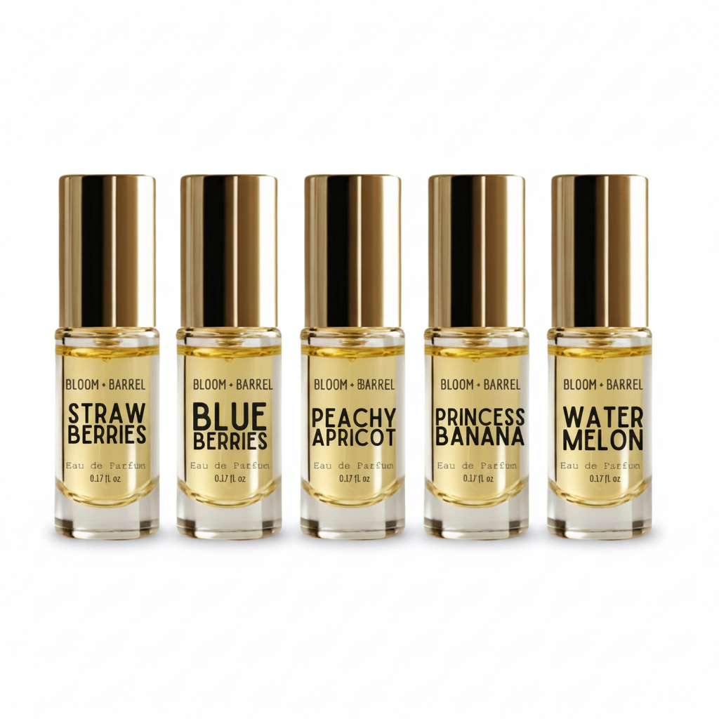 Five small glass perfume bottles with shiny gold caps arranged in a row on a white background. The labels read BLOOM + BARREL and the scents: Strawberries, Blueberries, Peachy Apricot, Princess Banana, and Watermelon.