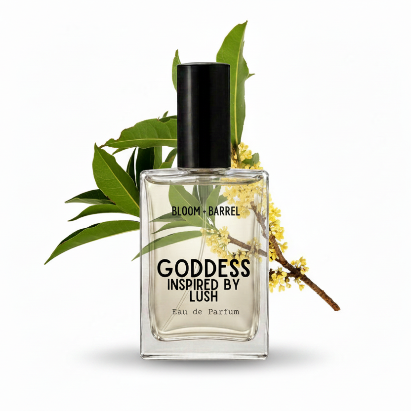 A rectangular glass perfume bottle labeled 'GODDESS INSPIRED BY LUSH' and 'BLOOM • BARREL' with a black cap, shown on a white background with green leaves and small yellow flowers behind it.