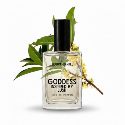 A rectangular glass perfume bottle labeled 'GODDESS INSPIRED BY LUSH' and 'BLOOM • BARREL' with a black cap, shown on a white background with green leaves and small yellow flowers behind it.