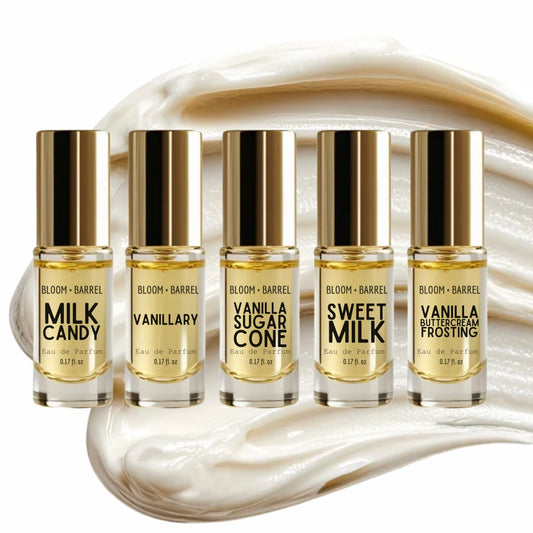 Five small perfume bottles with gold caps arranged in a row on a white background with a cream-colored whipped cream swirl behind them. The bottles are labeled with different vanilla and milk-flavored scents including Milk Candy, Vanilla, Vanilla Sugar Cone, Sweet Milk, and Vanilla Ice Cream Frosting.