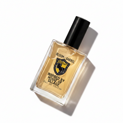 A rectangular glass bottle of Bloom Barrel Eau de Parfum with a black cap, filled with amber-colored liquid. The front label features a black and yellow shield logo with a horse, and text reading 'BLOOM • BARREL' and 'INSPIRED BY HOUSE OF SILLAGE'.