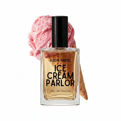 A rectangular glass perfume bottle labeled 'BLOOM • BARREL ICE CREAM PARLOR Eau de Parfum' with a black cap, shown in front of a pink ice cream scoop and waffle cone on a white background.