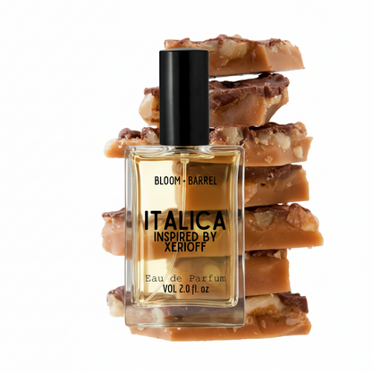 A rectangular glass perfume bottle labeled 'ITALICA INSPIRED BY XERIOFF' with a black cap, centered in front of stacked caramel-brown candy pieces on a plain white background.