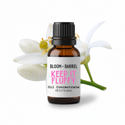 Bottle of 'Keep It Fluffy' oil concentrate by Bloom & Barrel with flowers in the background.