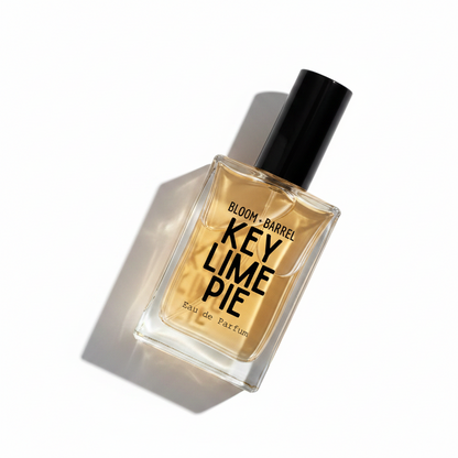 Bloom + Barrel Key Lime Pie Eau de Parfum in a rectangular clear glass bottle with a black cap, filled with golden-yellow fragrance liquid, on a plain white background.