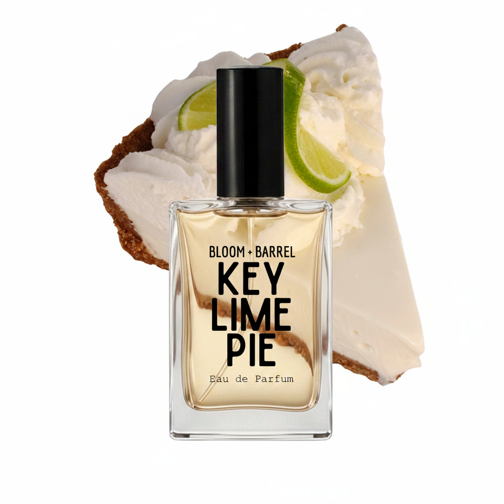 A rectangular glass perfume bottle labeled 'BLOOM + BARREL KEY LIME PIE Eau de Parfum' with a black cap, centered in front of a dessert slice with whipped cream, lime, and graham cracker on a white background.