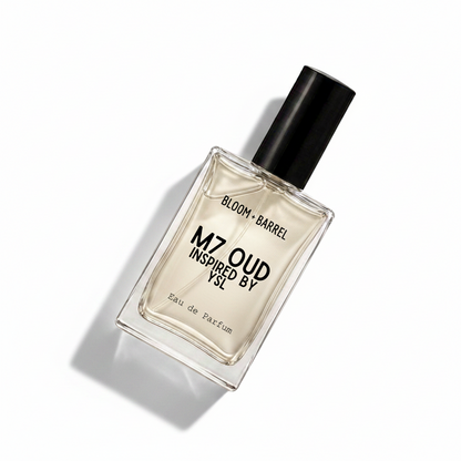 A rectangular glass perfume bottle with a black cap, containing a pale amber liquid. The front label reads 'BLOOM • BARREL' and 'M7 OUD INSPIRED BY YSL', with 'Eau de Parfum' at the bottom, on a plain white background.