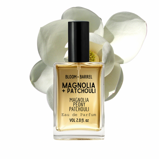 Perfume bottle labeled 'Bloom & Barrel Magnolia + Patchouli' with flowers in the background