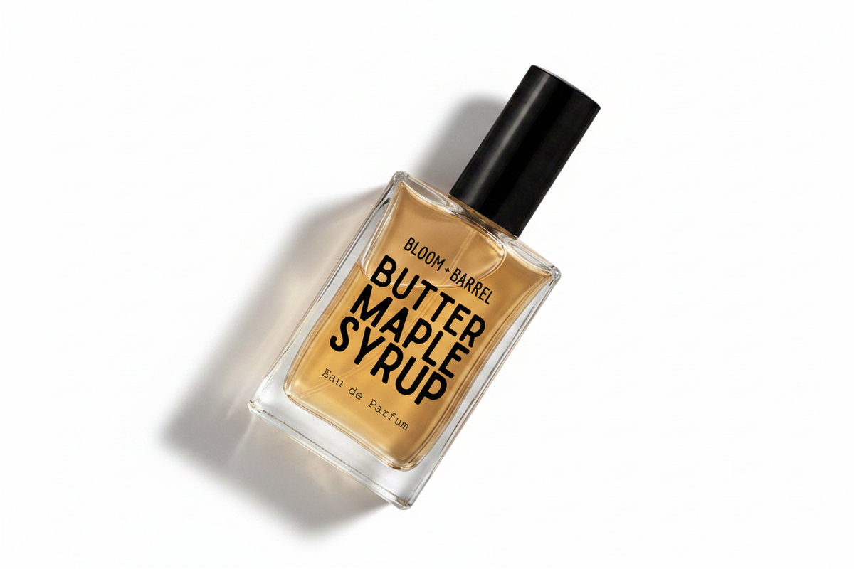 A rectangular glass bottle of Bloom + Barrel Butter Maple Syrup Eau de Parfum with a black cap, filled with amber-colored syrup, on a solid white background.