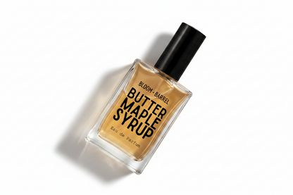 A rectangular glass bottle of Bloom + Barrel Butter Maple Syrup Eau de Parfum with a black cap, filled with amber-colored syrup, on a solid white background.