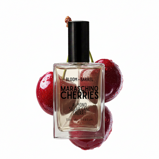 Bloom Barrel Maraschino Cherries Eau de Parfum bottle, featuring a clear glass bottle with a black cap, surrounded by three glossy red cherries on a white background.